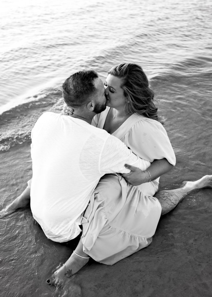 Family Photographer, man and woman have legs wrapped around each other as they kiss in beach sand