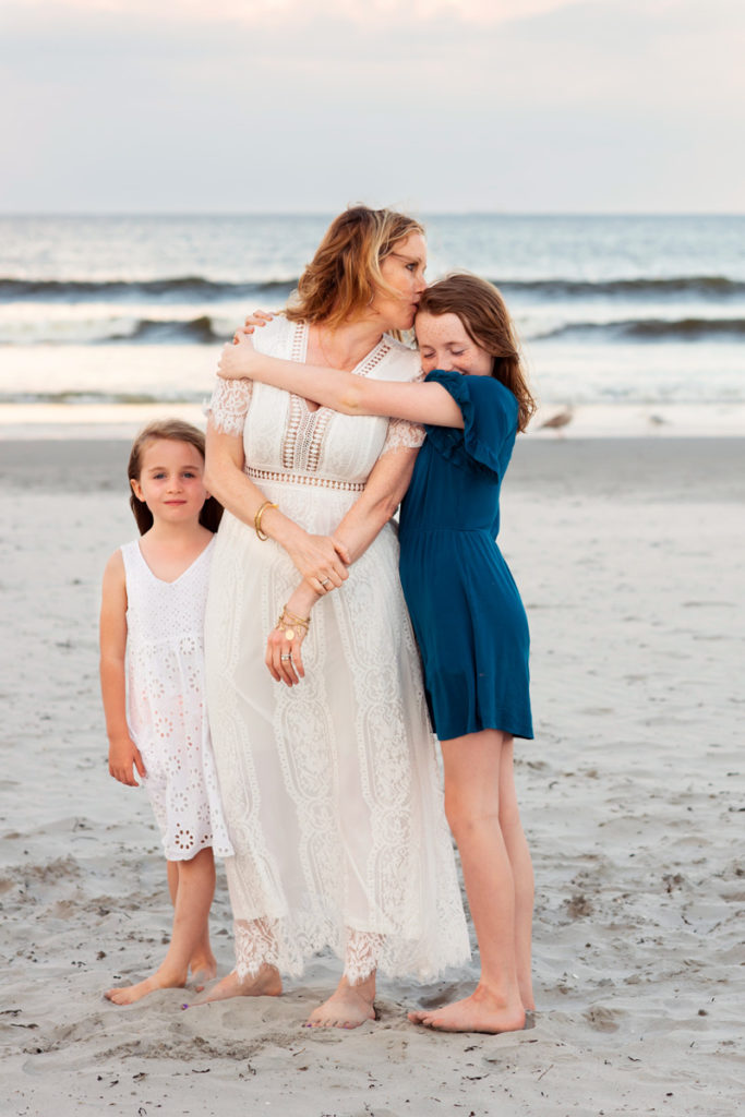 Family Photographer, daughters draw close to mom at the beach